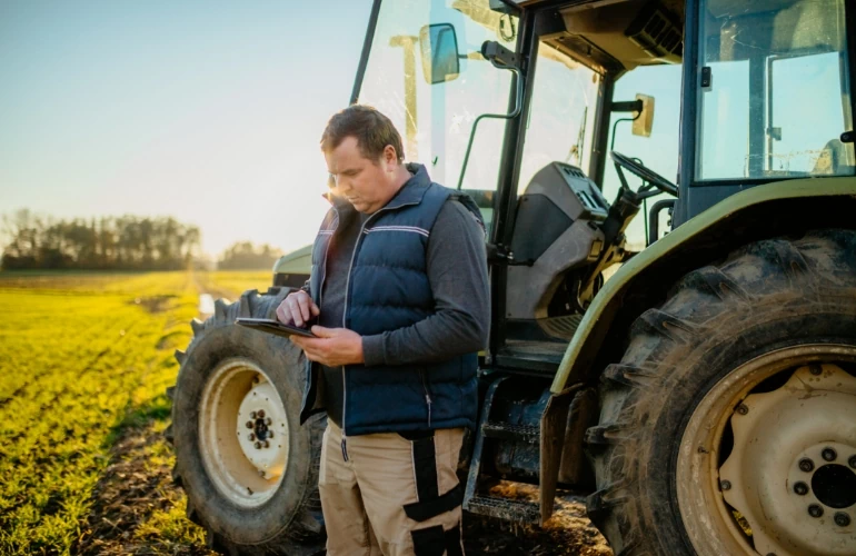 osoba stojąca przy traktorze z telefonem w dłoniach